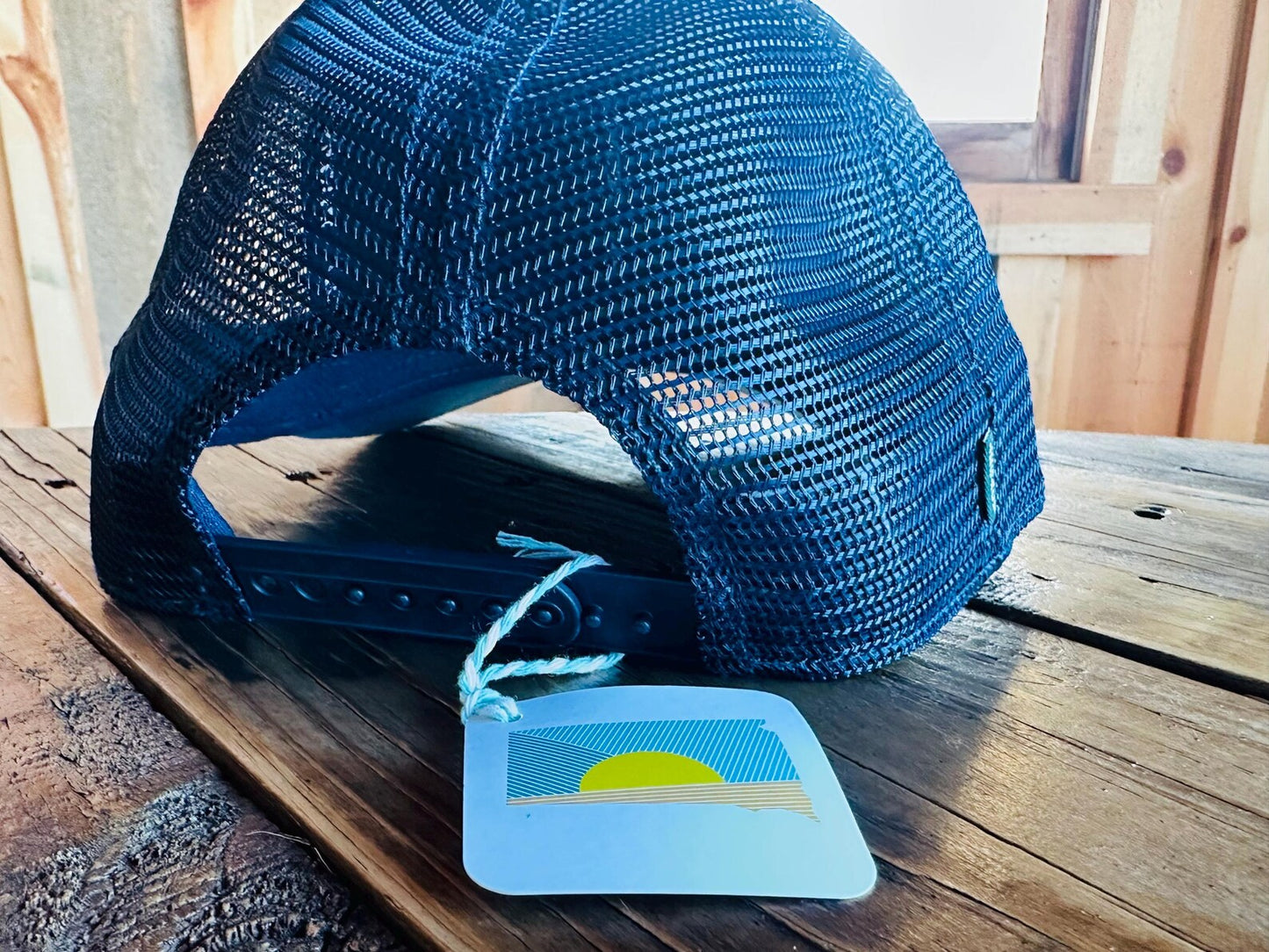 Blue mesh cap on a wooden surface with a matching blue tag featuring a sun design.