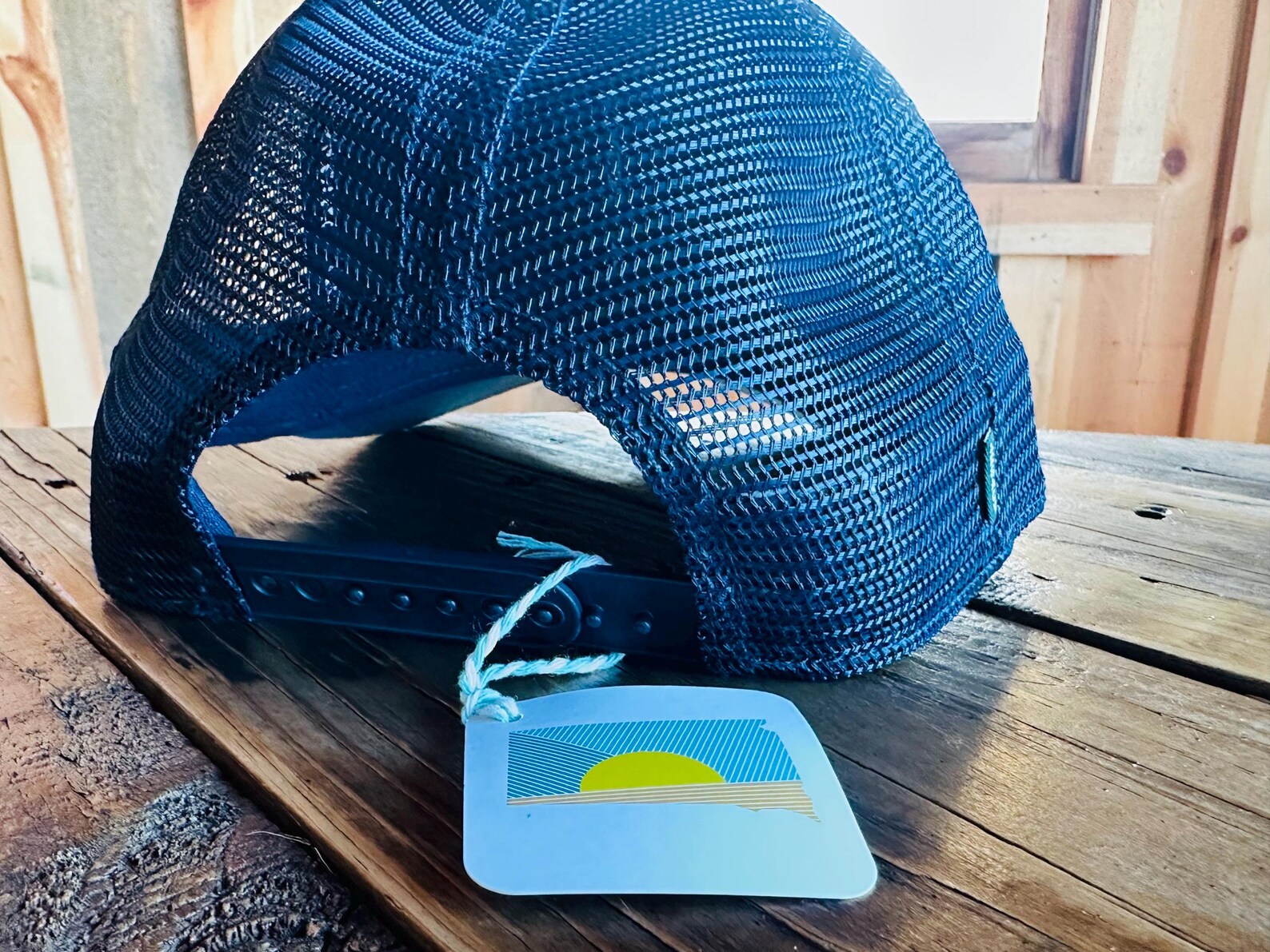 Blue mesh cap on a wooden surface with a matching blue tag featuring a sun design.